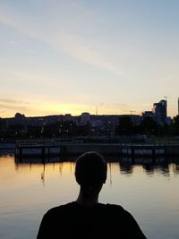 Rear view of silhouette woman by river against sky during sunset