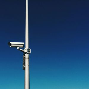 Low angle view of security camera against clear blue sky