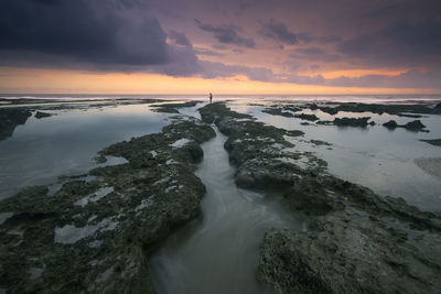 Scenic view of rocky shore and sea against sky during sunset