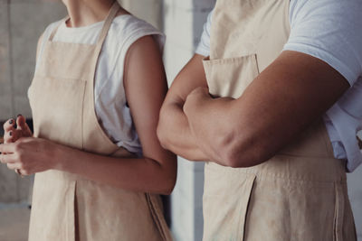 Midsection of people wearing aprons while standing against wall