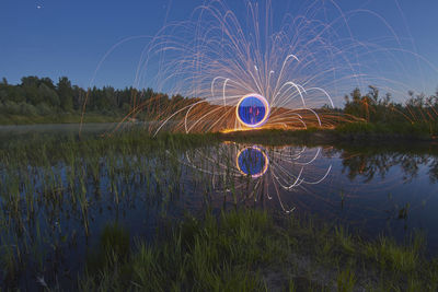 Light trails on field by lake against sky at night