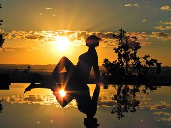 Silhouette woman by lake against sky during sunset