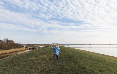 Girl standing at grassy lakeshore against sky