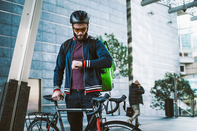 Man checking time while standing by bicycle outdoors