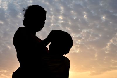 Silhouette mother and daughter standing against sky during sunset