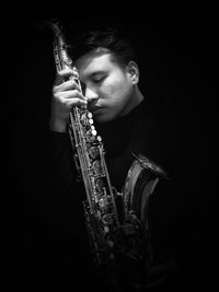 Man holding saxophone against black background