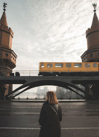 Rear view of woman against bridge with passing train