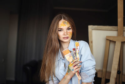 Portrait of female artist holding paintbrushes