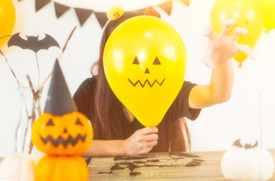 Woman holding yellow balloon with anthropomorphic face at table