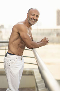 Portrait of shirtless man standing against railing