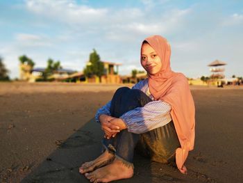 Portrait of smiling young woman sitting against sky