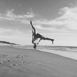 Young man jumping at beach against sky