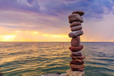 Stack of rocks on shore against sky during sunset