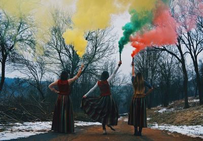 Rear view of women with distress flare standing on road during winter