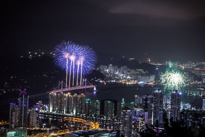 Fireworks display over illuminated cityscape and gwangan bridge against sky