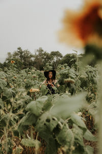 Young woman standing amidst sunflowers on field against sky