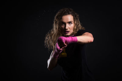 Portrait of female boxer standing against black background