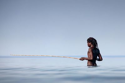 Shirtless man holding stick in sea