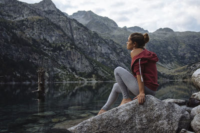 Woman with bun sitting on a rock by a lake during a trip.