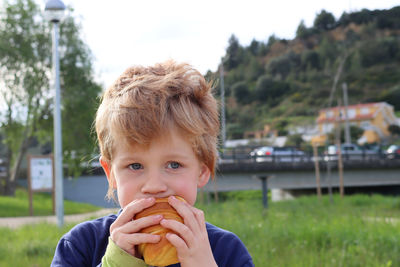 The blond boy takes a bite of a croissant and looks thoughtfully into the distance. serious boy.