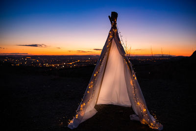 Illuminated tent on field against sky at sunset