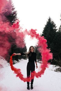 Portrait of young woman standing in park against sky during winter