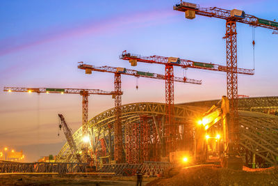 Low angle view of crane at construction site against sky during sunset