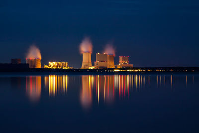 Illuminated smoke emitting from factory against sky at night