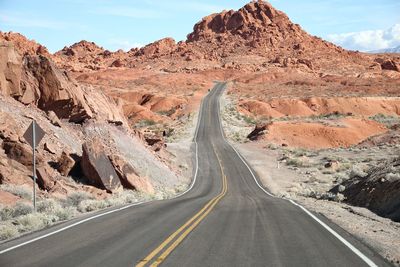 Empty road leading towards rocky mountains during sunny day