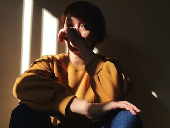 Portrait of young woman sitting against wall at home