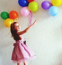 Full length of smiling woman standing against multi colored balloons