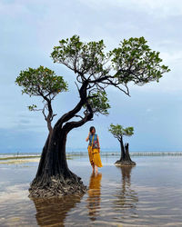 A woman standing near a tree that grows above the sea