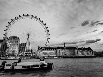 Ferris wheel by river against sky in city