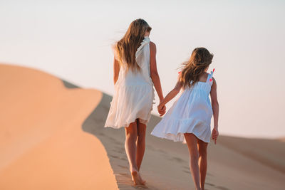 Rear view of women walking on sand at beach