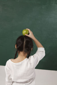 Rear view of girl holding granny smith apple