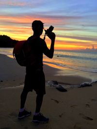 Man photographing sea against sky during sunset