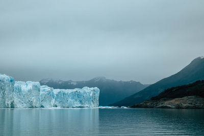 Lake and glacier against snowcapped mountains and cloudy sky