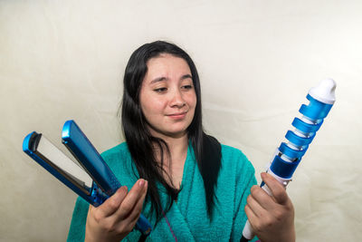 Close-up of young woman holding curling tongs and hair straightener