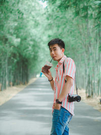 Portrait of young man having drink while standing on road