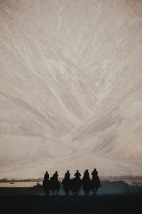 Silhouette people riding camel on mountain road