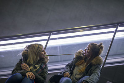 Female friends eating food while sitting on escalator