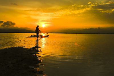 Silhouette woman standing in sea against sky during sunset