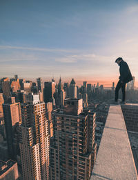 Rear view of man standing on terrace by cityscape against sky during sunset