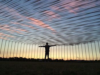 Silhouette man standing on field against sky at sunset