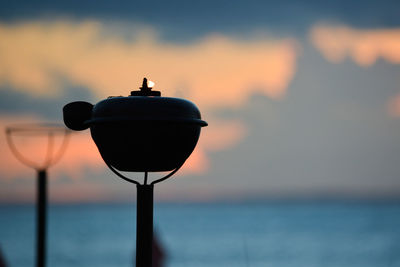 Silhouette lamp by sea against sky during sunset