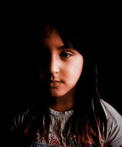 Close-up portrait of young woman against black background