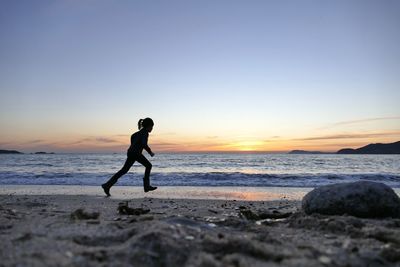 Full length of girl running at beach against sky during sunset