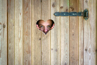 Close-up portrait of man peeking through heart shape on wooden door