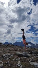 Woman jumping on beach against cloudy sky