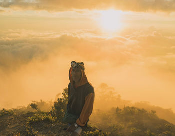 Mature man standing on mountain against cloudy sky during sunset